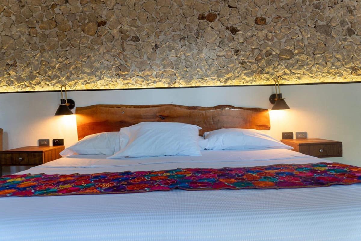 A bed with white linens and a colorful blanket, a wooden headboard, and two bedside lamps.