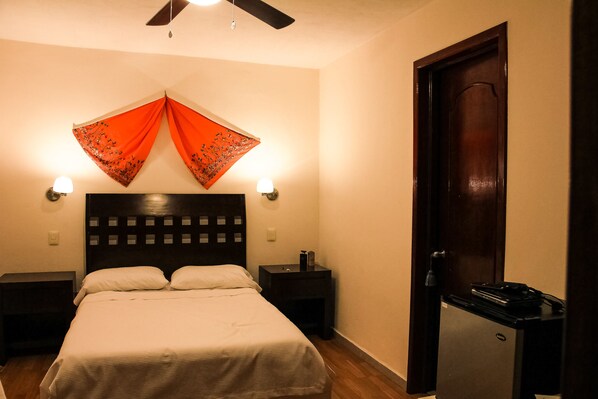 Una habitación de hotel con una cama, dos mesitas de noche, un ventilador de techo y una puerta.