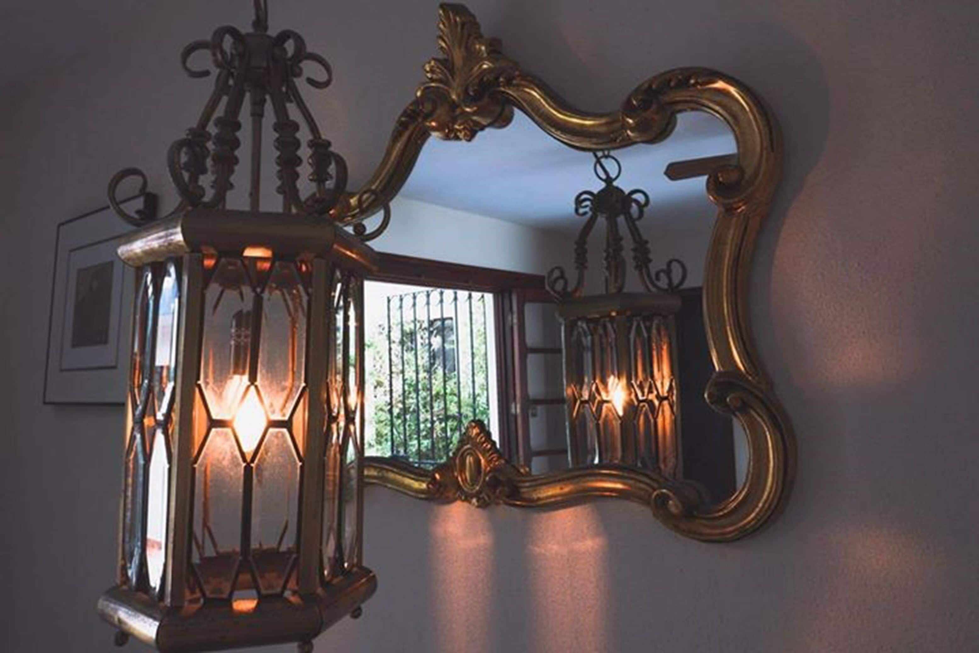 Un espejo fijado a la pared con un marco decorativo y un farol colgante con varias luces.