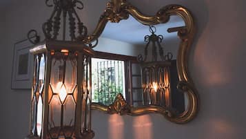 Un espejo fijado a la pared con un marco decorativo y un farol colgante con varias luces.