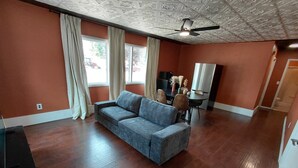A room with a sofa, a ceiling fan, a television, and a dining table with chairs. - Arrowhead Motel (Sundance)