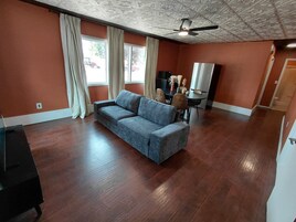 A room with a sofa, a ceiling fan, a television, and a dining table with chairs.