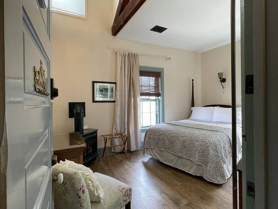 Un dormitorio con cama, una silla, un escritorio y una ventana con cortinas.