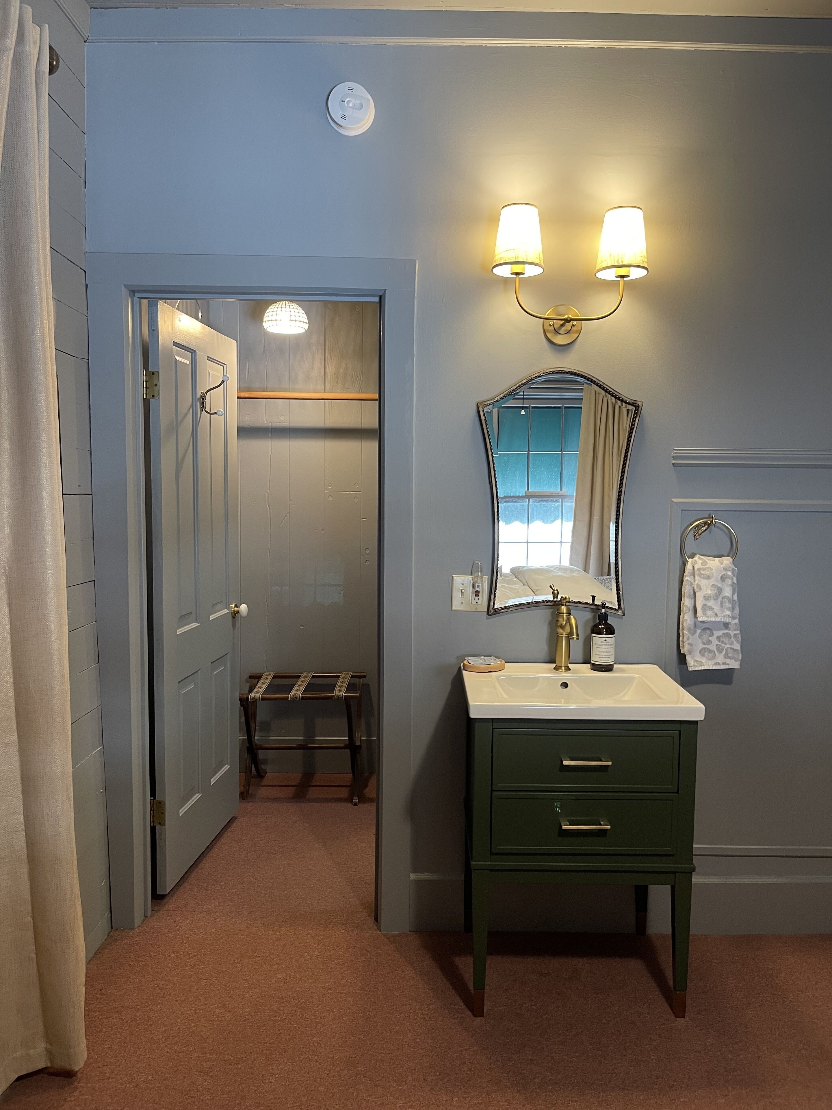 A bathroom with a green vanity, a mirror, a wall-mounted light fixture, and a towel rack.