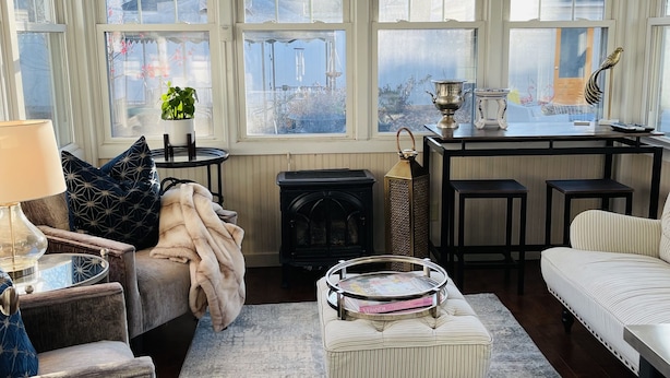 A cozy living room with a fireplace, a sofa, a coffee table, and a view through large windows. - Carriage House B&B (Winona)