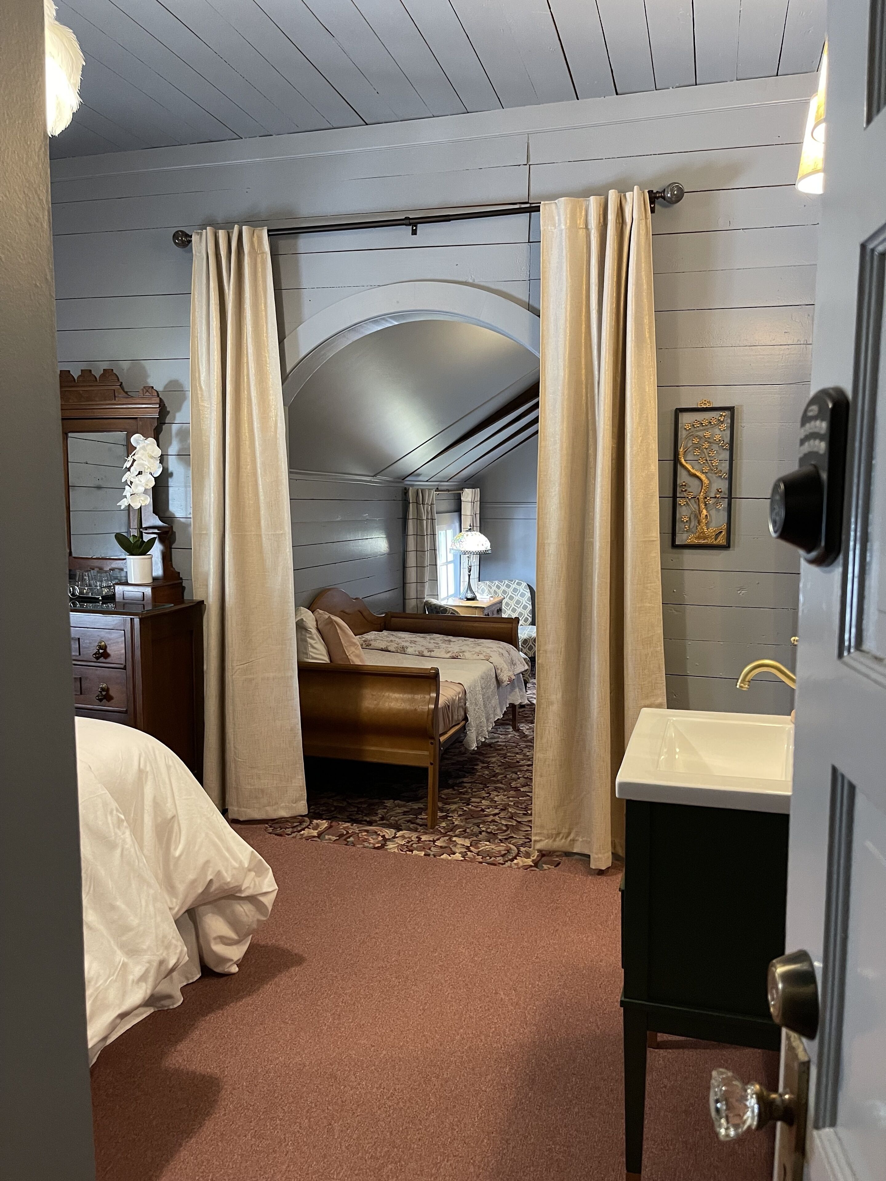 A bedroom with a bed, a dresser, a vanity, and a door with a lock.
