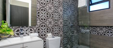 Un baño moderno con baldosas estampadas, un inodoro, un lavamanos con espejo y una ventana.