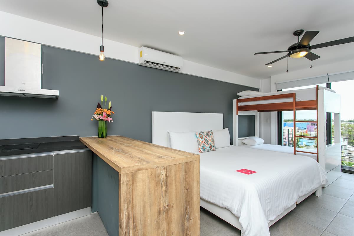 Ein modernes Hotelzimmer mit einem Holztisch, einem Bett mit weißer Bettwäsche, einem Deckenventilator und Blick auf die Stadt.