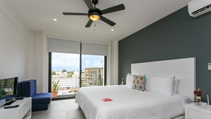 A modern hotel room with a large bed, a ceiling fan, a TV, and a balcony with a city view. - Studio 30 Condhotel by Nah Hotels (Playa del Carmen)