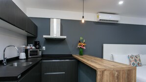 A modern kitchen with dark cabinetry, a wooden island, a built-in microwave, and a coffee maker. - Studio 30 Condhotel by Nah Hotels (Playa del Carmen)