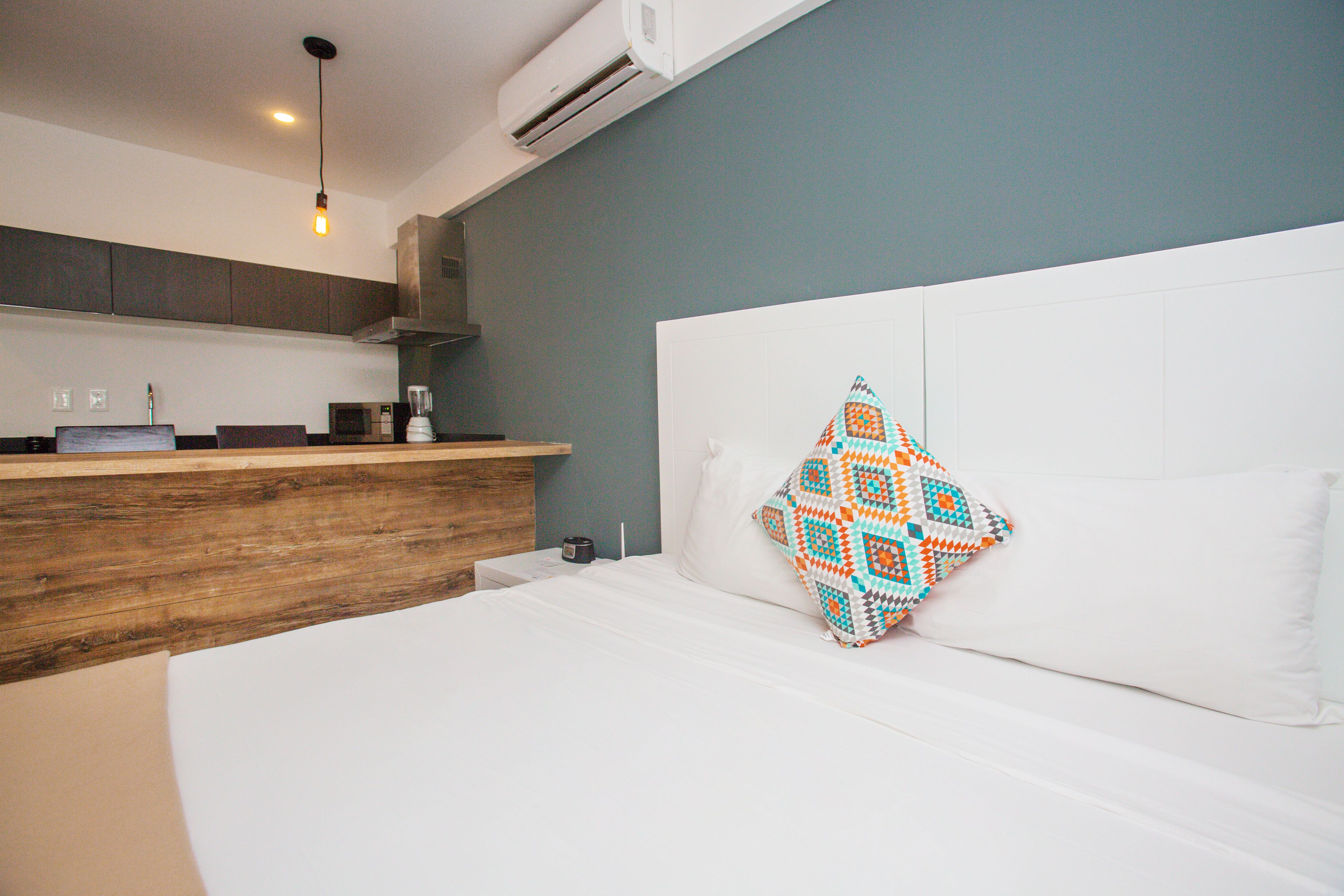 A modern hotel room with a wooden counter, a white bed, and a patterned pillow.