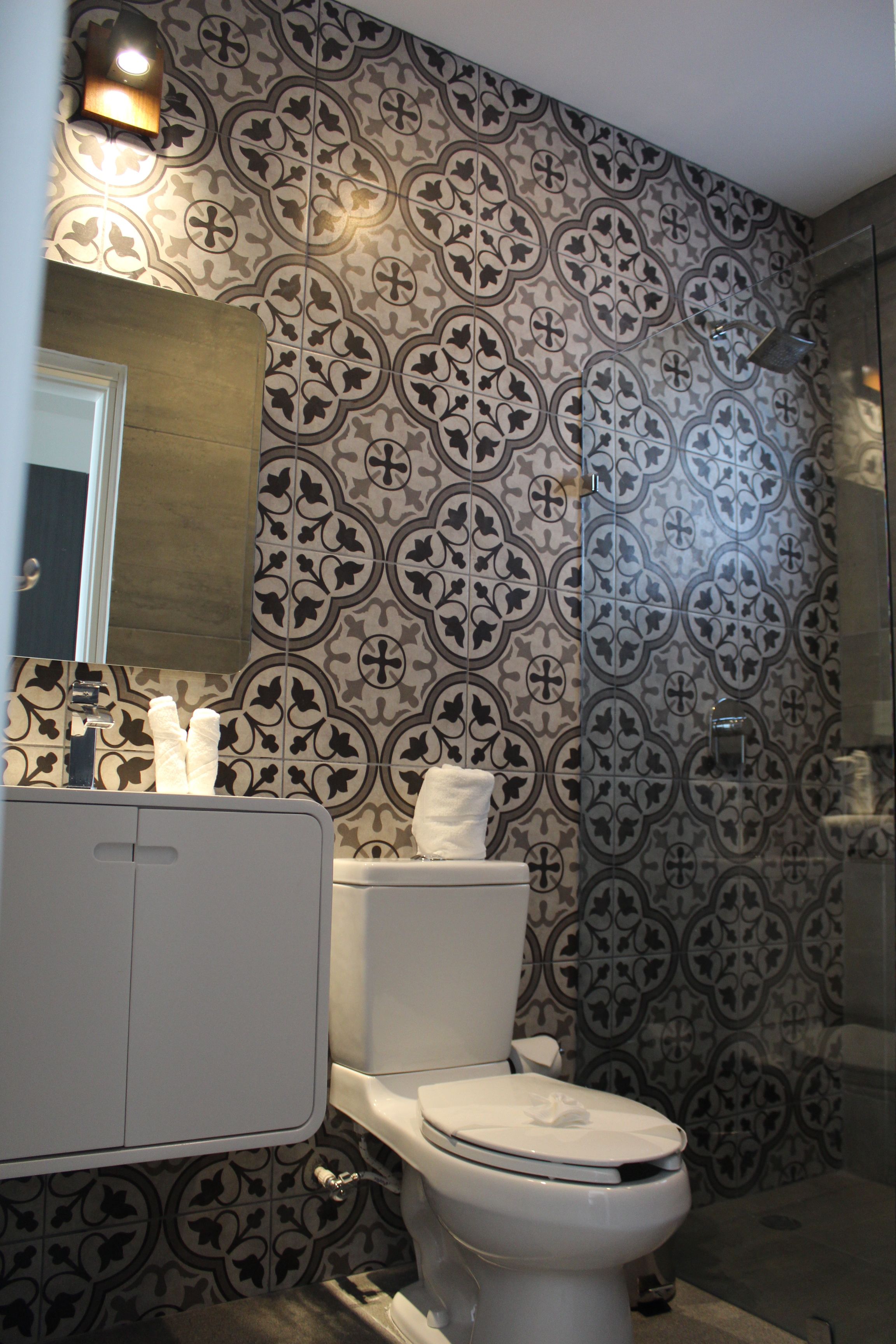 A bathroom with patterned tile walls, a white toilet, and a mirror above the sink.