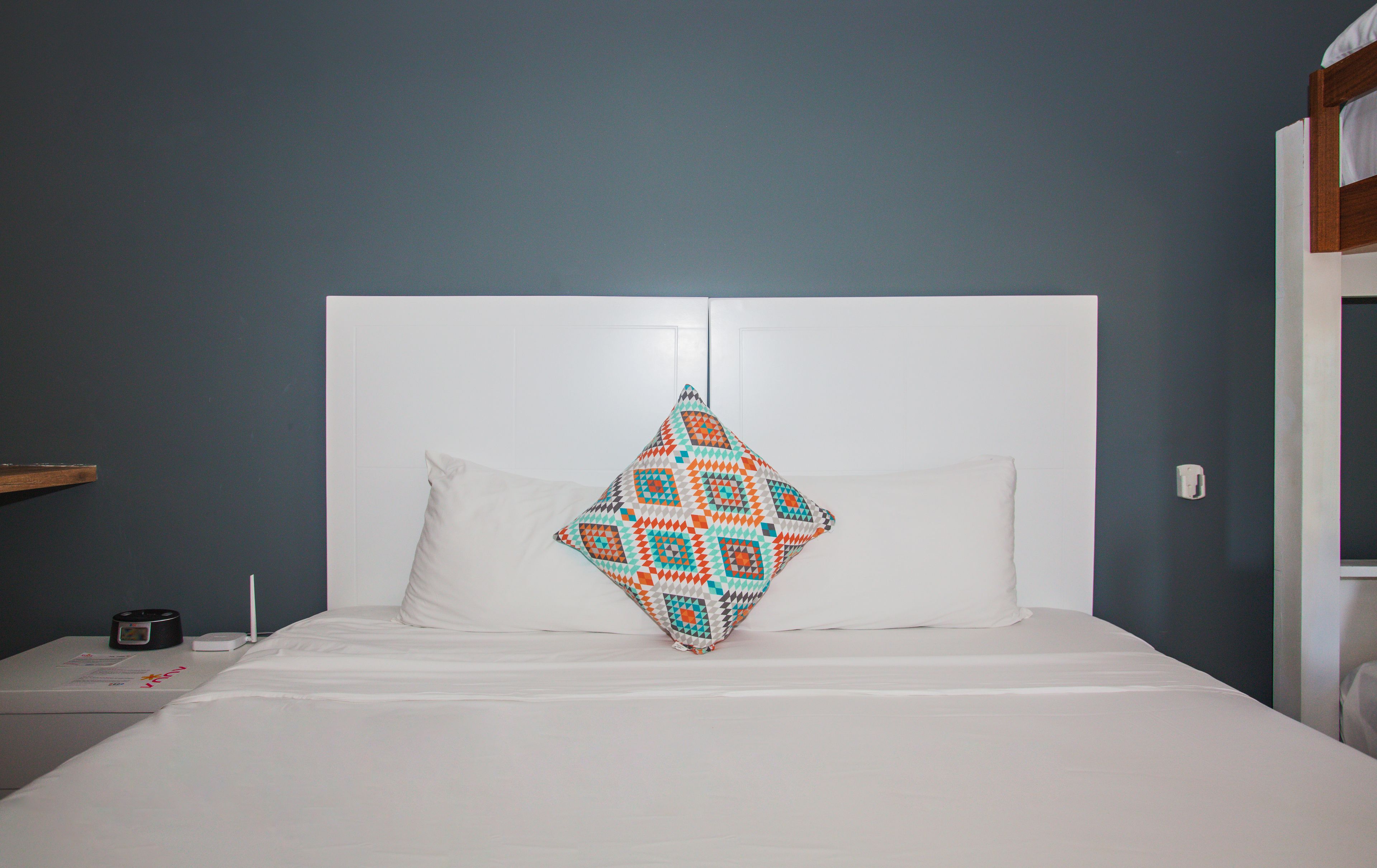 Un lit avec une tête de lit blanche, un oreiller blanc uni et un oreiller aux motifs géométriques colorés.