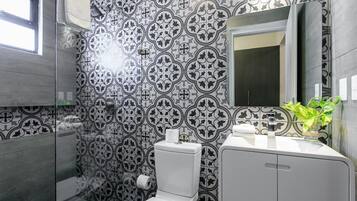 A bathroom with a patterned tile wall, a toilet, a sink with a mirror, and a window.