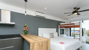 A modern hotel room with a wooden desk, a bed with white bedding, a ceiling fan, and a view of the city. - Studio 30 Condhotel by Nah Hotels (Playa del Carmen)