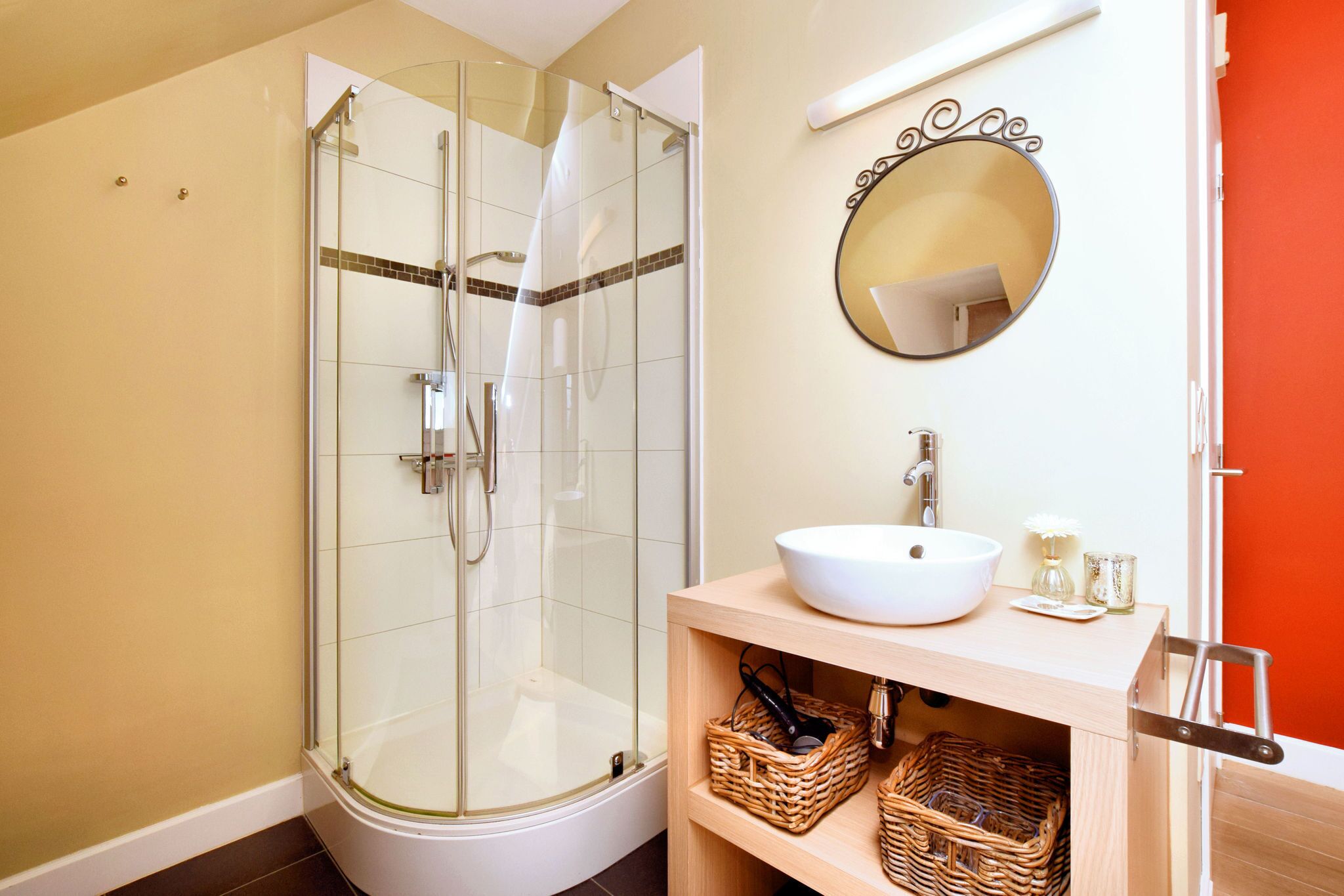 A bathroom with a glass-enclosed shower, a white sink, and wicker baskets on a wooden shelf.