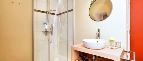 A bathroom with a glass-enclosed shower, a white sink, and wicker baskets on a wooden shelf.