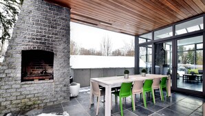 Une cheminée en pierre, un plafond en bois, une porte en verre, une table et des chaises.