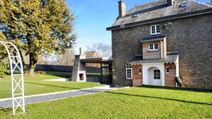 Un bâtiment en pierre avec une extension moderne, une pelouse bien entretenue et un arbre.