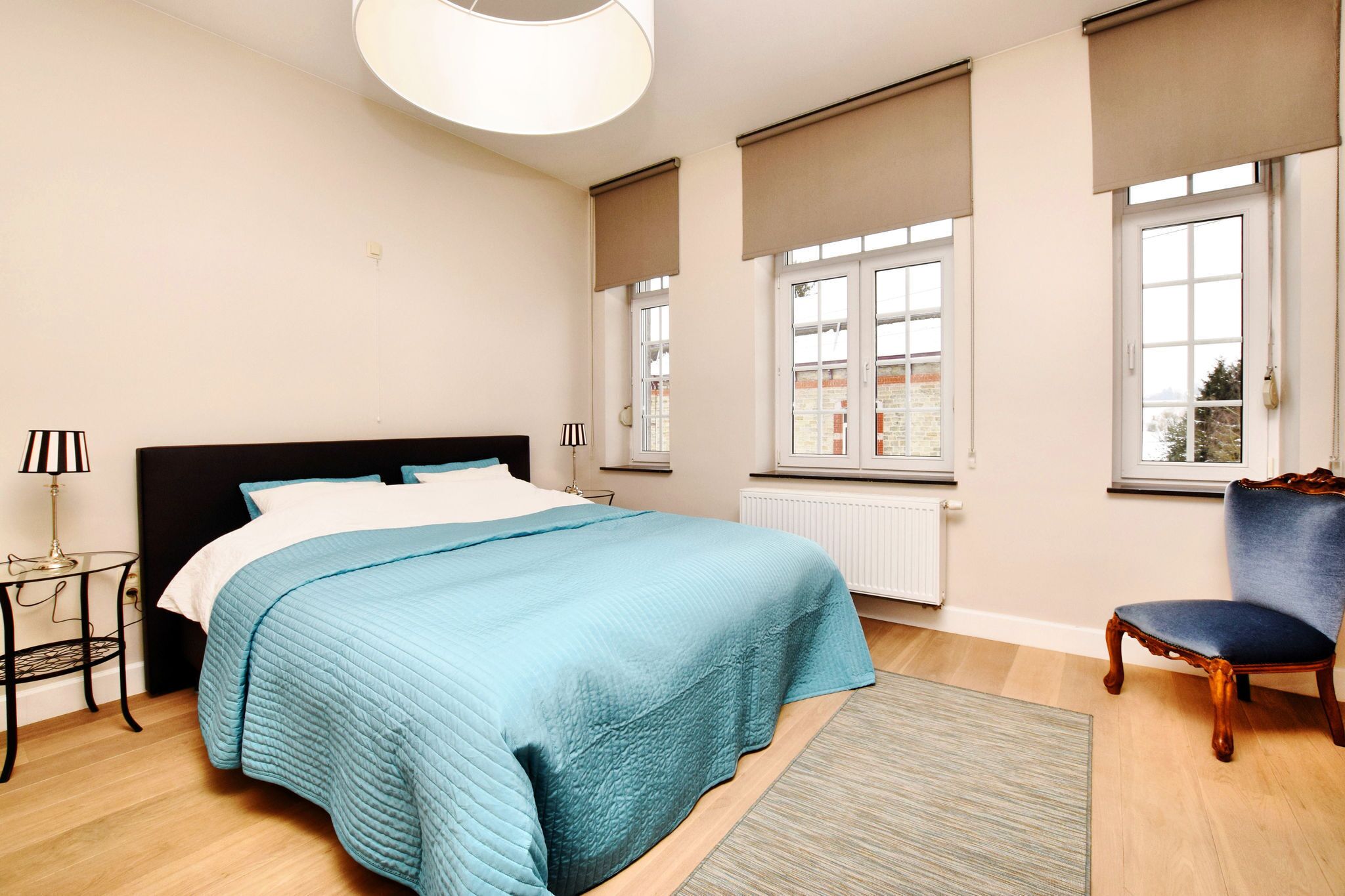 A bedroom with a bed, a chair, a lamp, and a window with blinds.