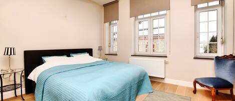 A bedroom with a bed, a chair, a lamp, and a window with blinds.