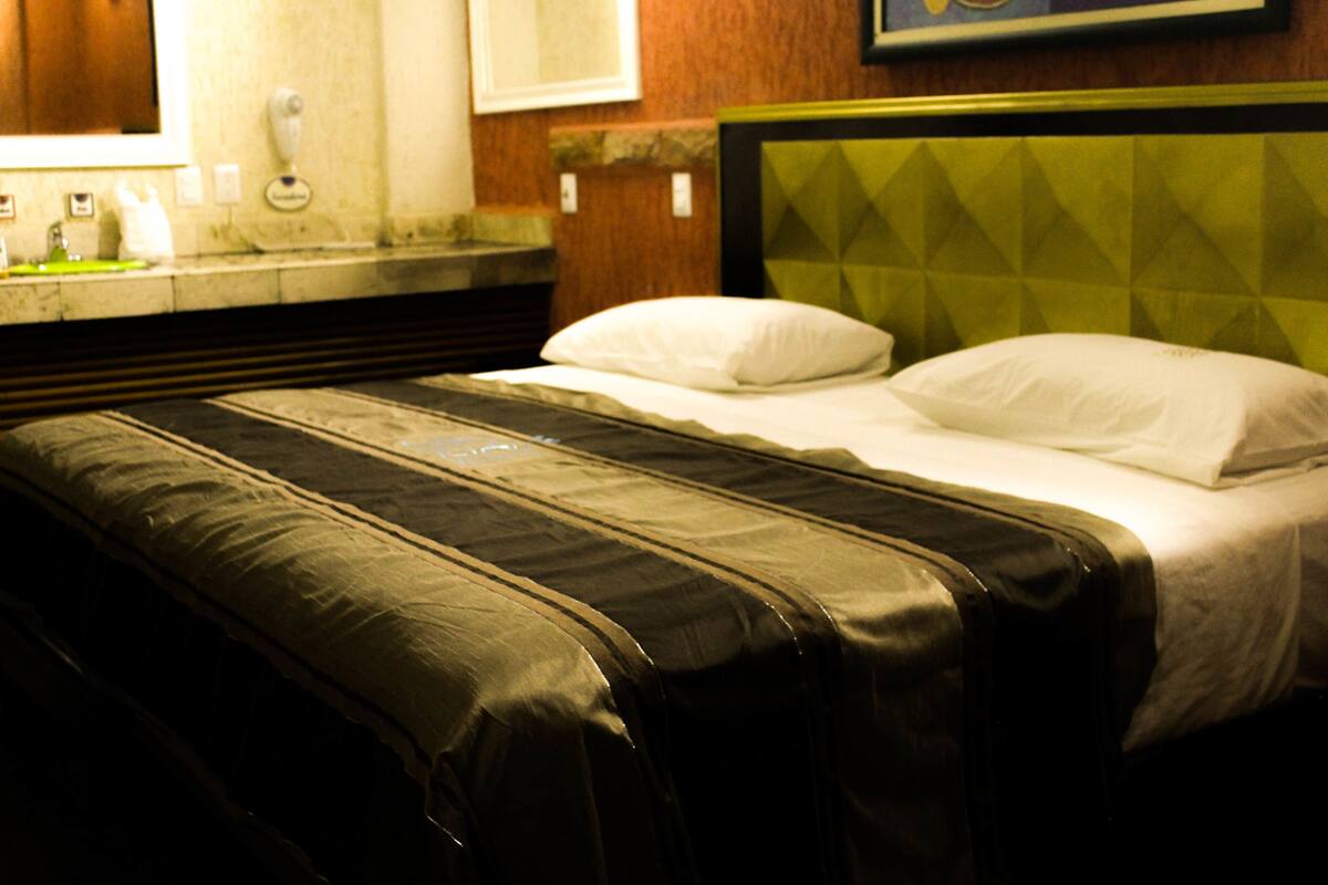 A hotel room with a bed, a headboard, a nightstand, and a mirror.