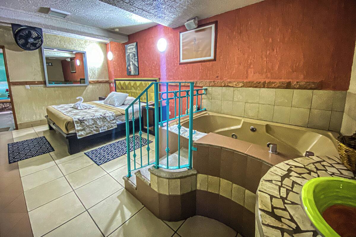 A hotel room with a bed, a bathtub, a small balcony, and a bathroom with a sink and mirror.