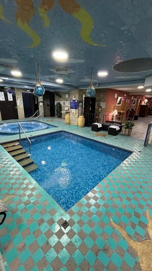 An indoor swimming pool with a checkered floor pattern, a hot tub, and a ceiling with a wave design.