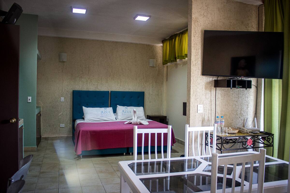 A hotel room with a bed, a TV, a table with chairs, and a window with curtains.