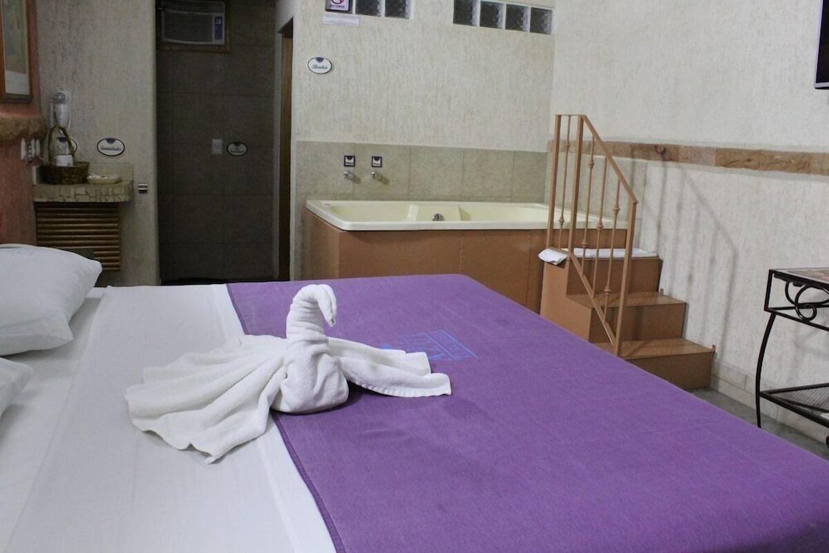 A hotel room with a bed, a bathroom with a bathtub, and a staircase.