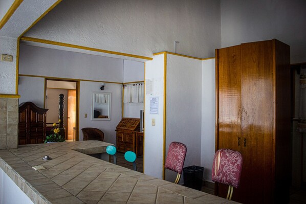 A room with a wooden wardrobe, a tiled counter, and a chair with a floral pattern.