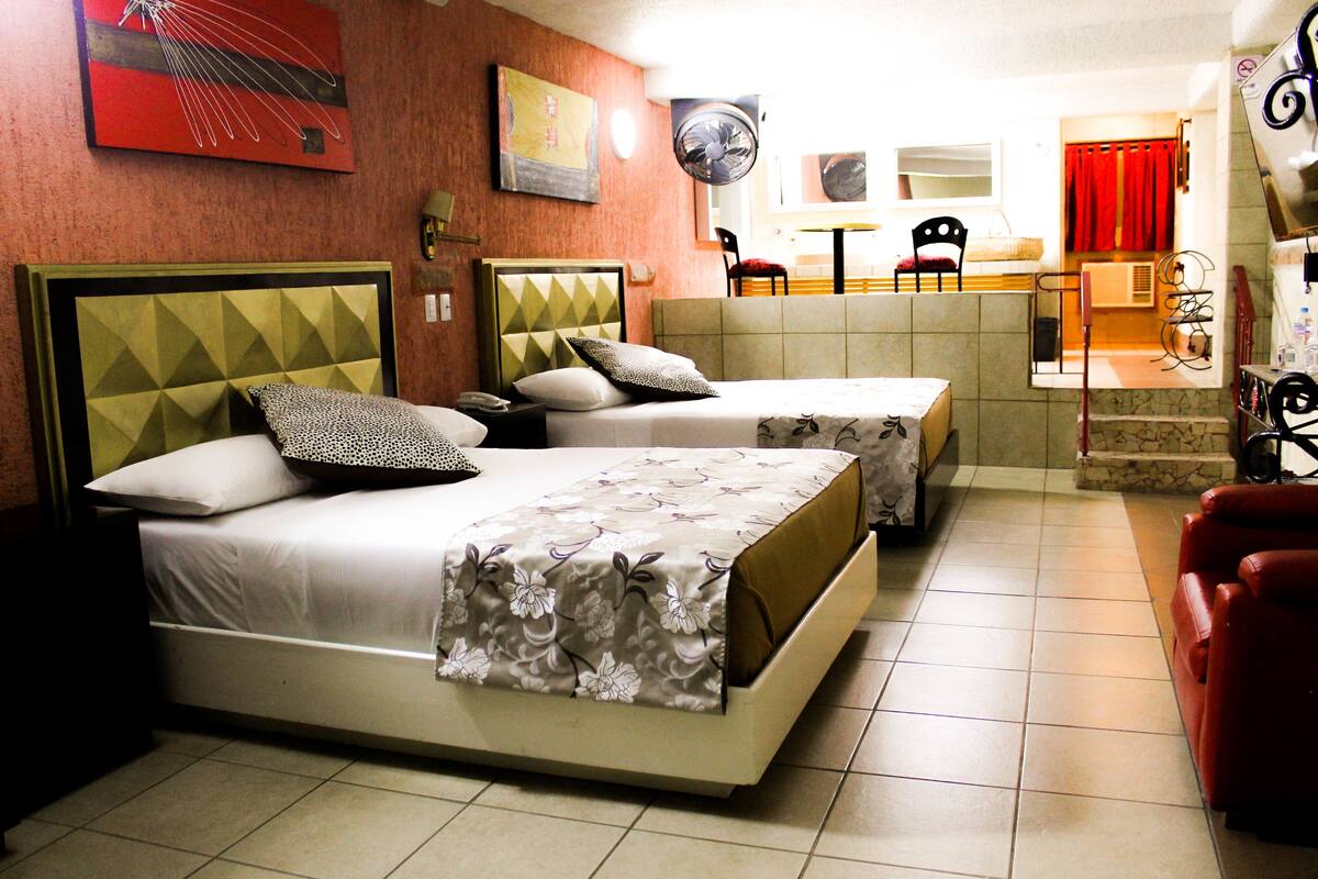 A hotel room with two beds, a dining area, and a red couch.