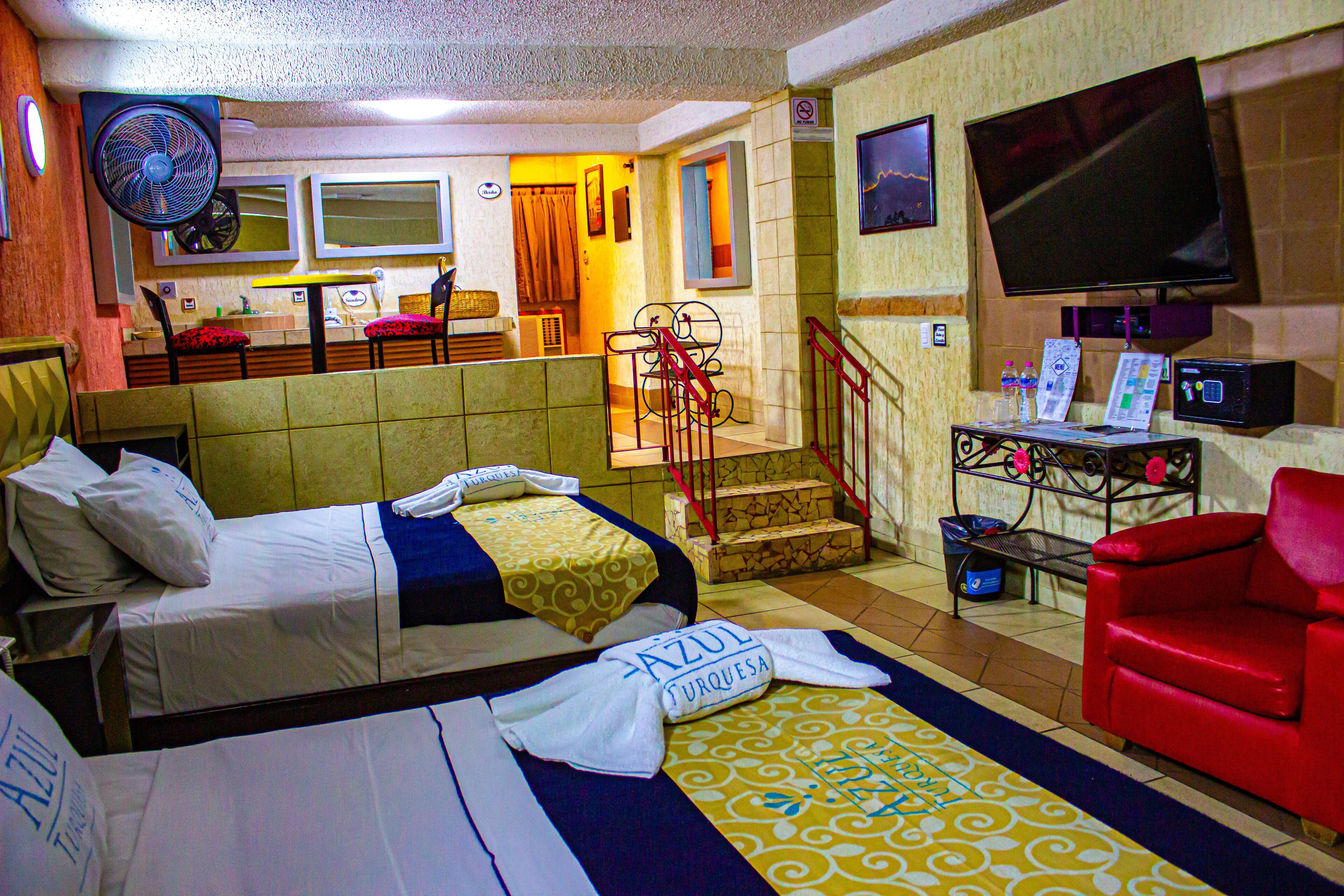 Een hotelkamer met twee bedden, een rode bank, een televisie en een bureau met een computer.