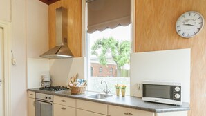 Una cucina con piano cottura, microonde e una finestra che si affaccia su un edificio in mattoni e alberi.