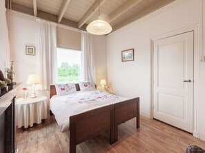 Ein Schlafzimmer mit einem hölzernen Bett, zwei Nachttischen mit Lampen, einem Fenster mit Vorhängen und einer Tür.