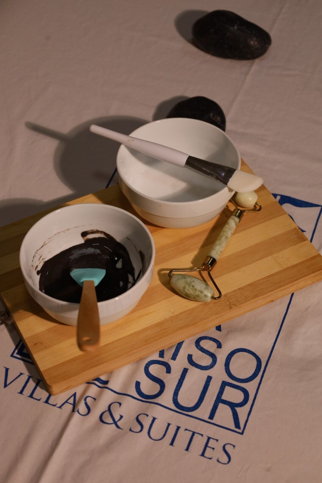 Una tabla de madera con un tazón de chocolate, una cuchara y un rodillo de mármol sobre una mesa con una toalla que dice 'VILLAS & SUITES'.