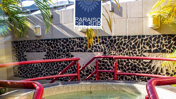 Uma banheira de hidromassagem com grades vermelhas, cercada por azulejos de mosaico e uma placa com o nome 'Paraiso del Sur Villas & Suites'.
