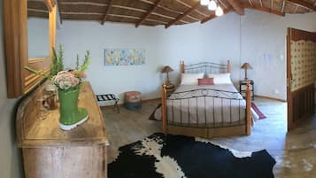 A bedroom with a bed, a wooden dresser, a cowhide rug, a painting, and a mirror.