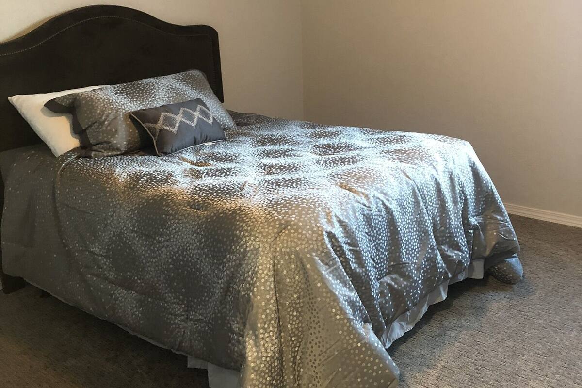 A bedroom with a bed, a headboard, and a carpeted floor.