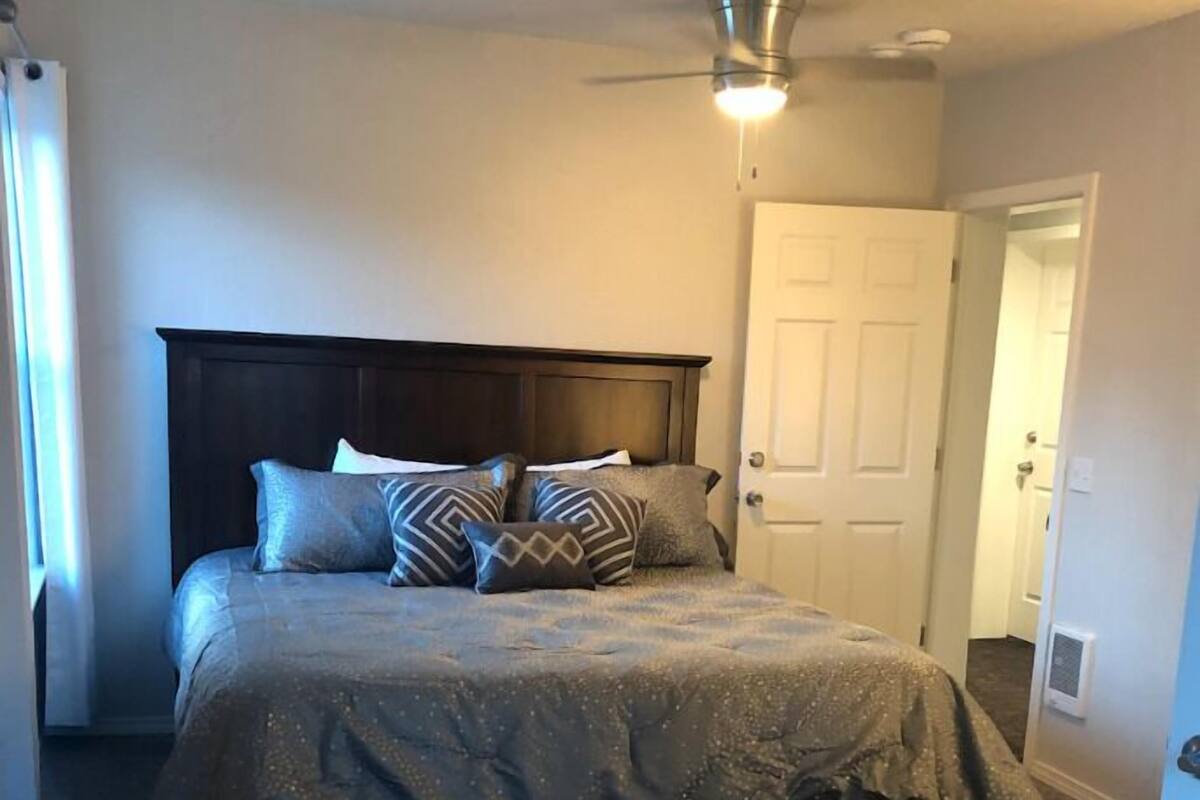 A bedroom with a bed, a ceiling fan, a door, and a patterned rug.