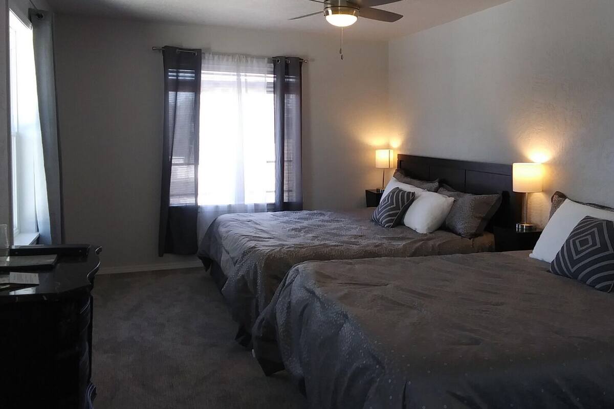 A hotel room with two beds, a desk, and a ceiling fan.