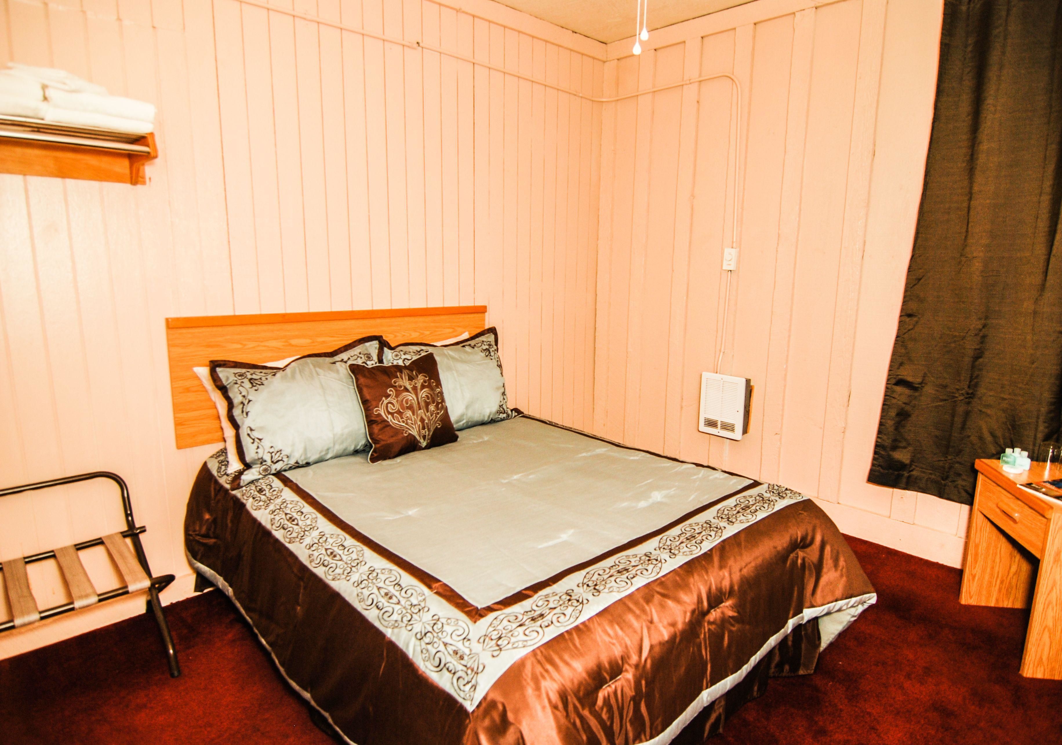 A bedroom with a bed, a wooden headboard, a bedside table, and a window with a curtain.