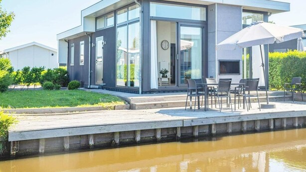 A modern house with a patio, a water body in front, and a clear sky. - Drenthe Family Getaway w/ Garden (West-Graftdijk)