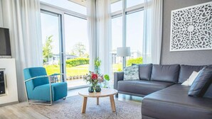 A modern living room with a sofa, a blue armchair, a coffee table, and a large window with a view of greenery. - Drenthe Family Getaway w/ Garden (West-Graftdijk)