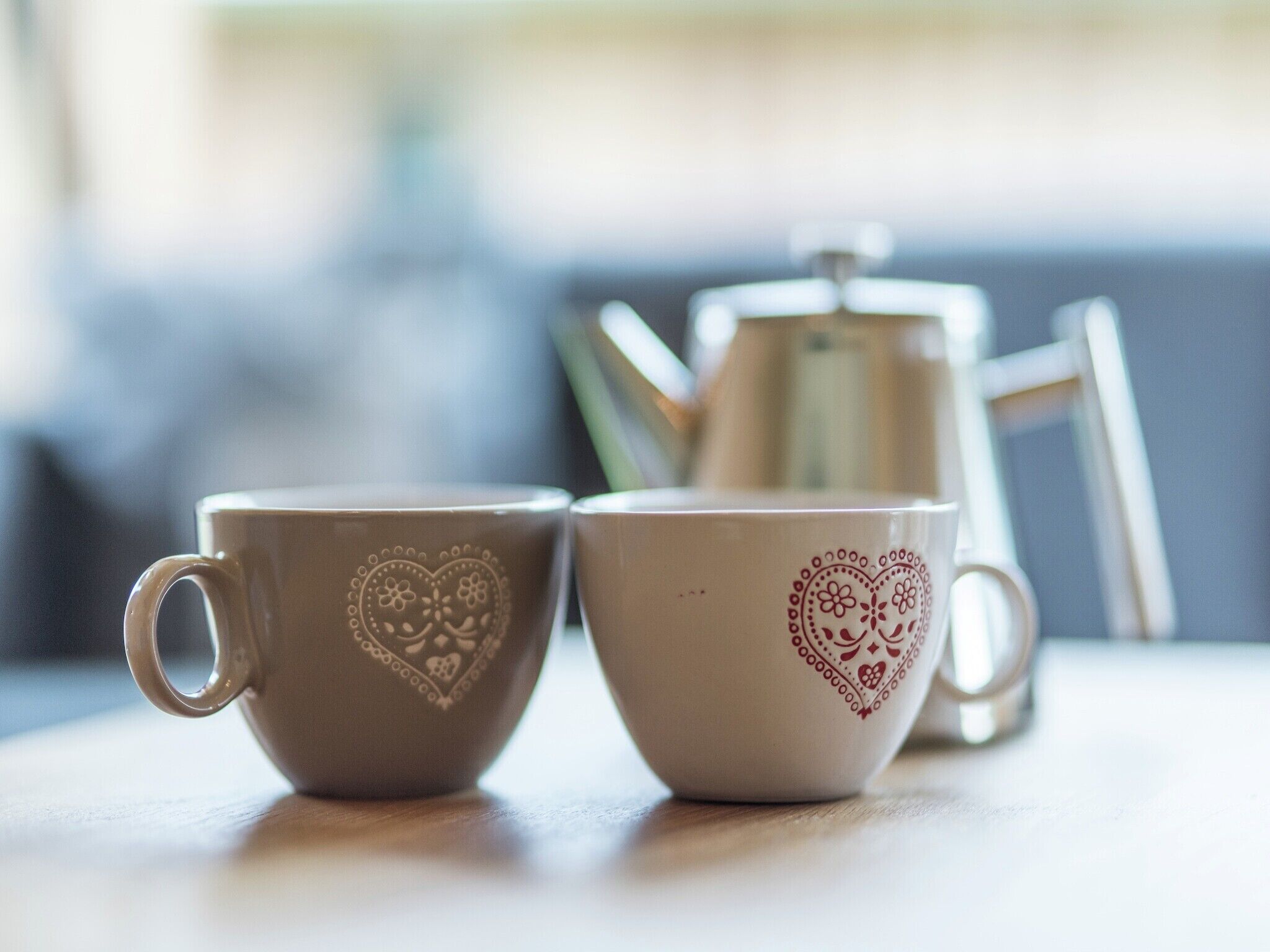 Deux tasses ornées de motifs en forme de cœur, posées sur une table.