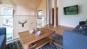 A modern interior with a wooden ceiling, a glass railing, a coffee table with cups, a mounted TV, and a sofa.