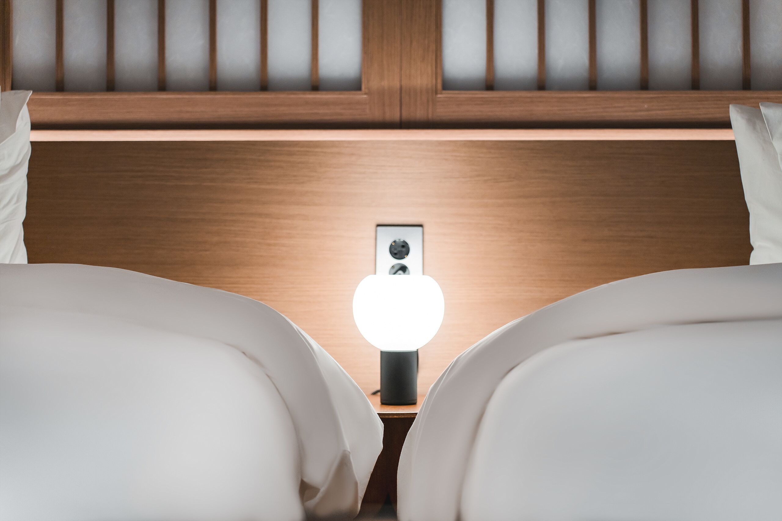 A hotel room with two beds, a wooden headboard, and a bedside table with a lamp.