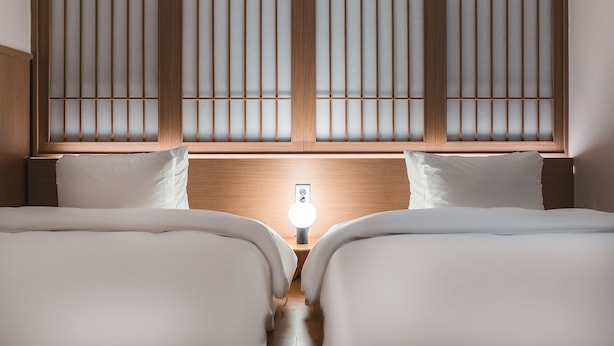 A hotel room with two beds, a wooden headboard, and a bedside table with a lamp.