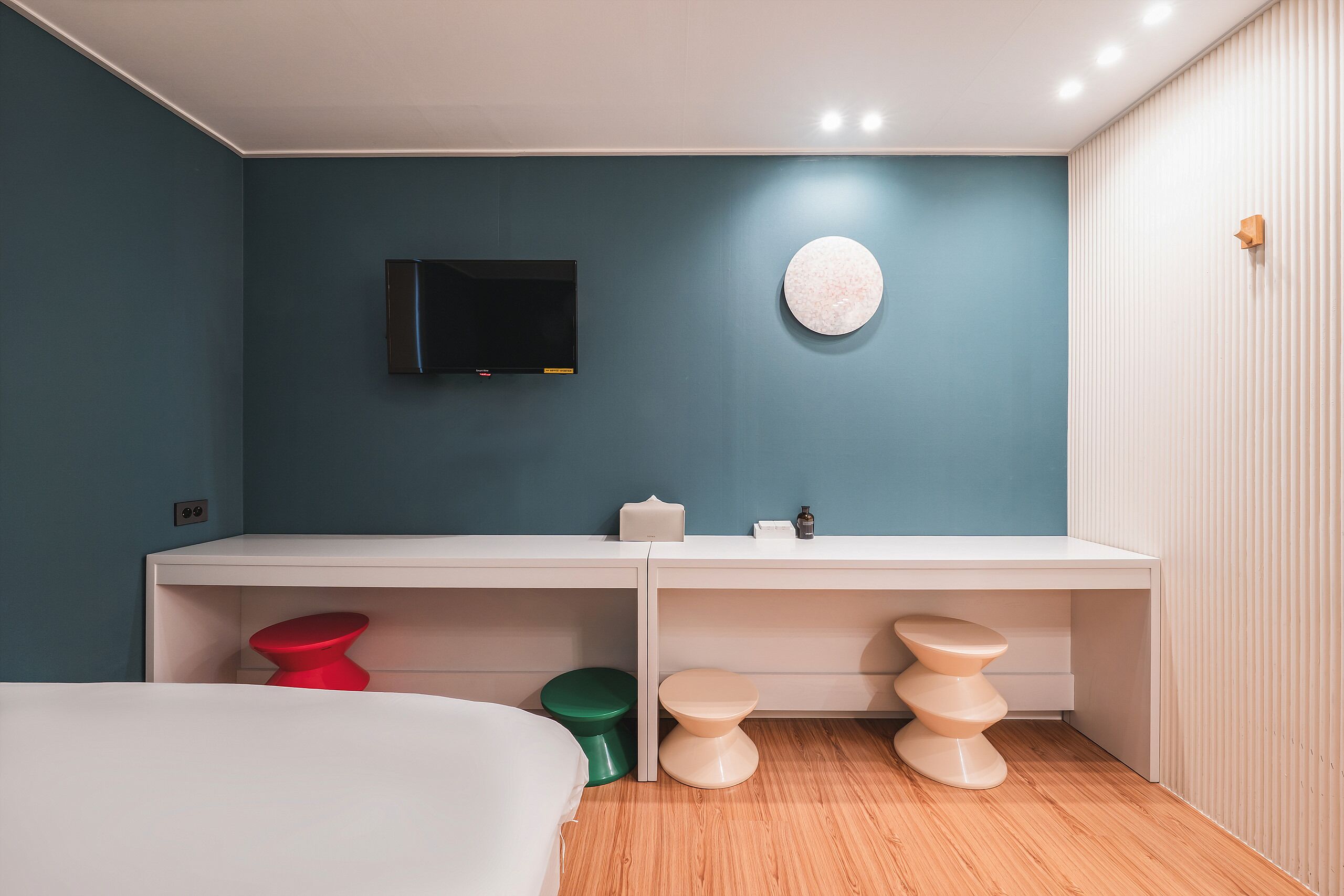 A modern bedroom with a bed, a white desk, a television, and a round wall decoration.