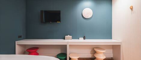 A modern bedroom with a bed, a white desk, a television, and a round wall decoration.
